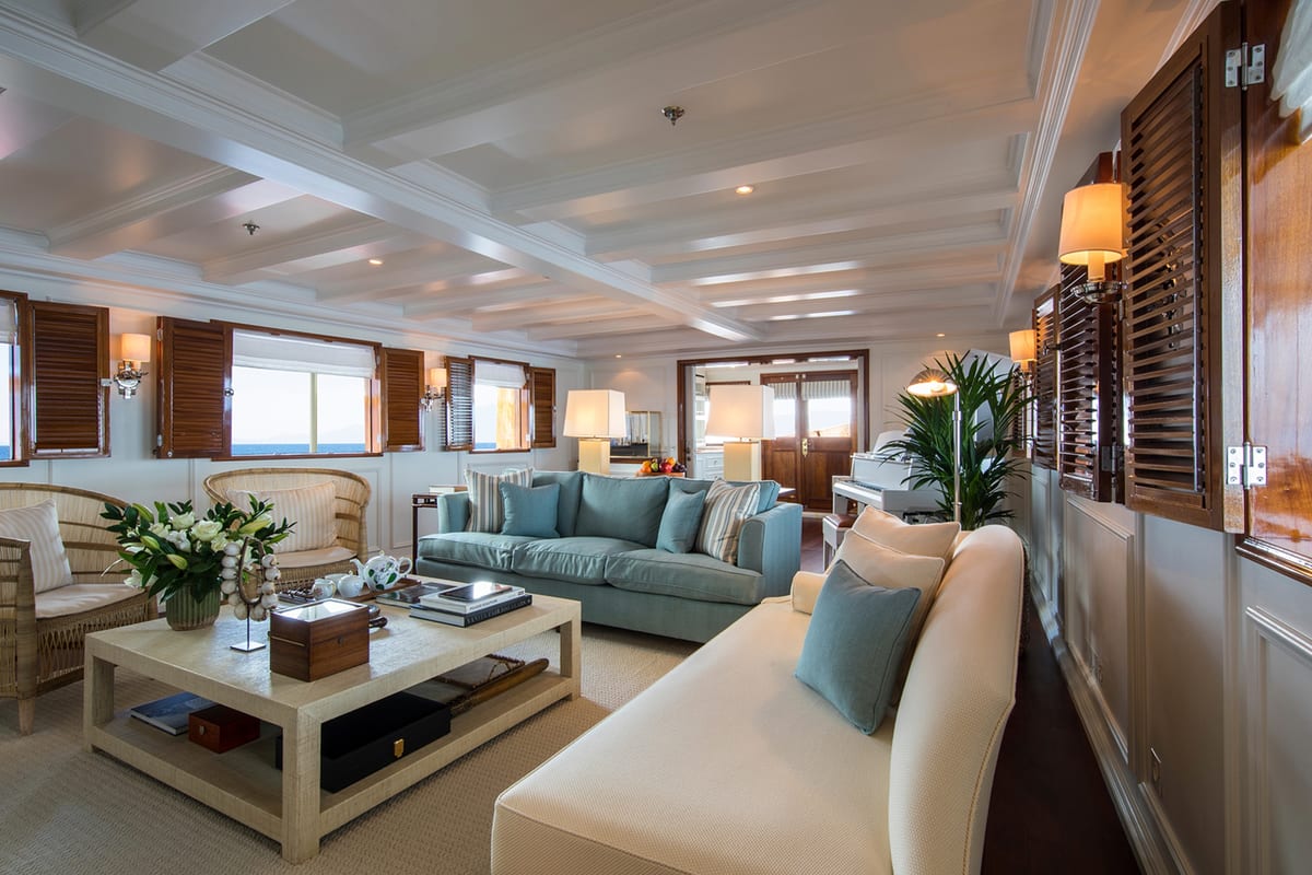 Refined main salon on Haida 1929 with soft-toned furnishings, timber shutters, and a white grand piano.