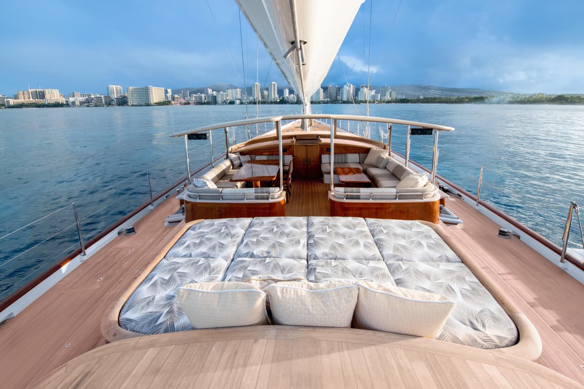 Spacious foredeck lounge on Halekai with sunpads and dining areas, overlooking Honolulu skyline.