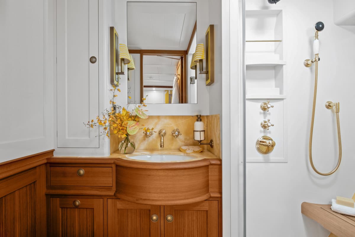 Superyacht Halekai’s guest bathroom with varnished wood cabinetry, stone basin surround and brass shower fittings.