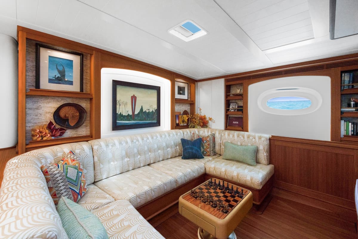 Halekai's cozy lounge with patterned corner sofa, chessboard table, sea view porthole, and island-themed artwork.