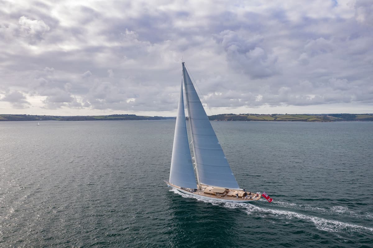 Halekai under sail in Falmouth Bay, Cornwall, with dramatic skies and rolling headlands in the background.