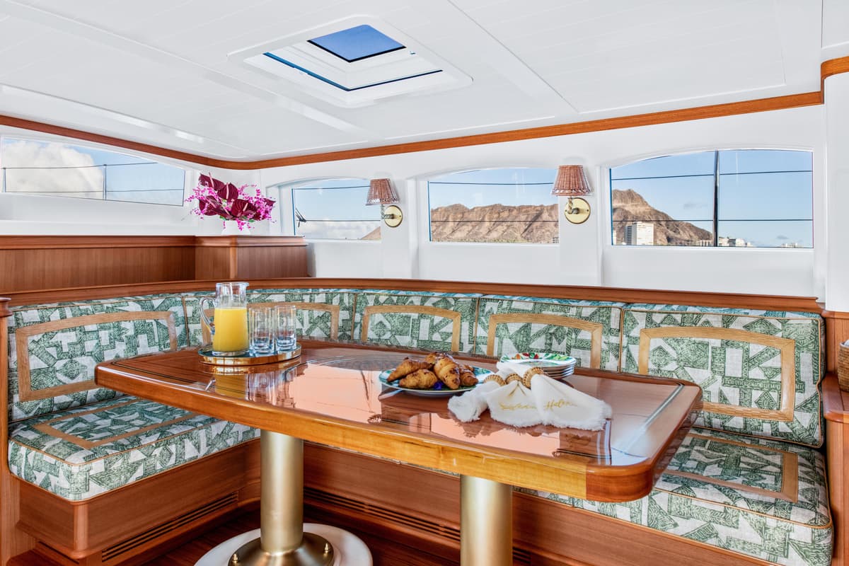 Indoor dining nook aboard Halekai with patterned seating, breakfast spread, and Diamond Head views.