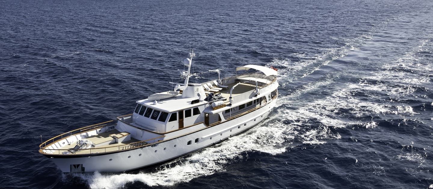 Classic motor yacht Heavenly Daze cruising through the Mediterranean with coastal hills in the background.