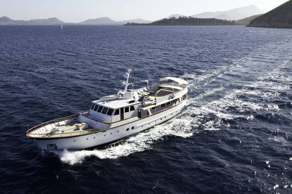 Classic motor yacht Heavenly Daze cruising through the Mediterranean with coastal hills in the background.