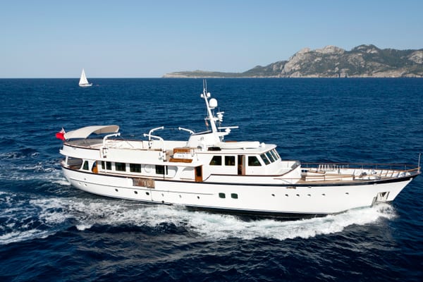 Classic motor yacht Heavenly Daze cruising in the Mediterranean with coastal mountains in the background.
