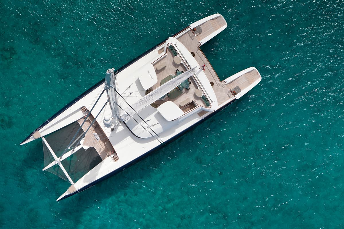 Aerial view of Hemisphere, the world’s largest sailing catamaran, anchored over clear turquoise water.