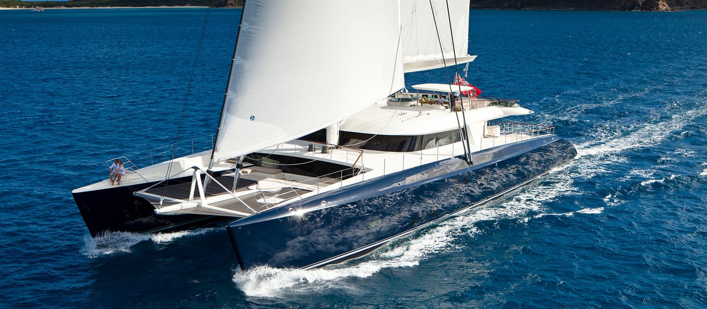 Luxury sailing catamaran Hemisphere gliding through tropical waters with sails raised and guests relaxing on deck.
