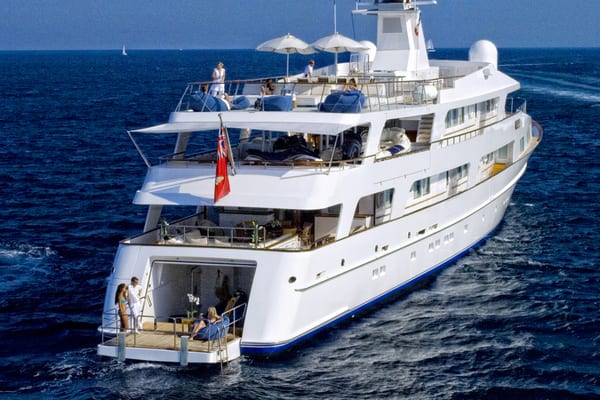 Aft view of Illusion at sea showing tender garage and multiple deck levels with guests relaxing.
