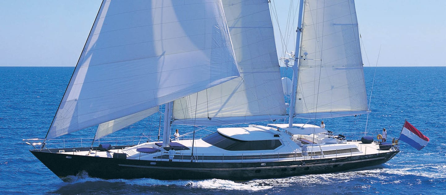 Sailing yacht La Cattiva underway with full sails, cutting through open water under clear blue skies.
