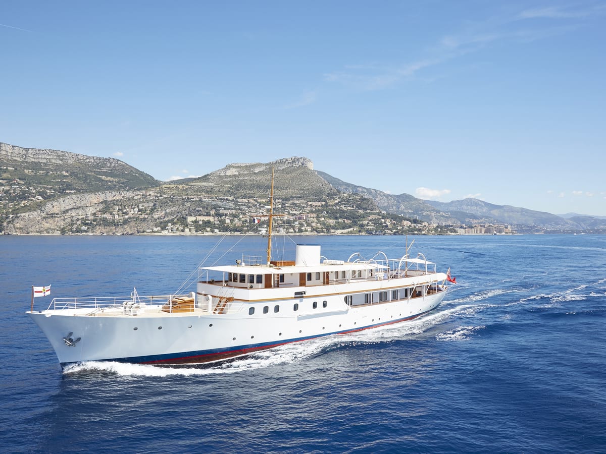 Classic motor yacht Malahne cruising along the Mediterranean coast, showing her restored profile and white bimini frame.