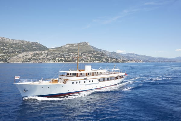 Classic motor yacht Malahne cruising along the Mediterranean coast, showing her restored profile and white bimini frame.