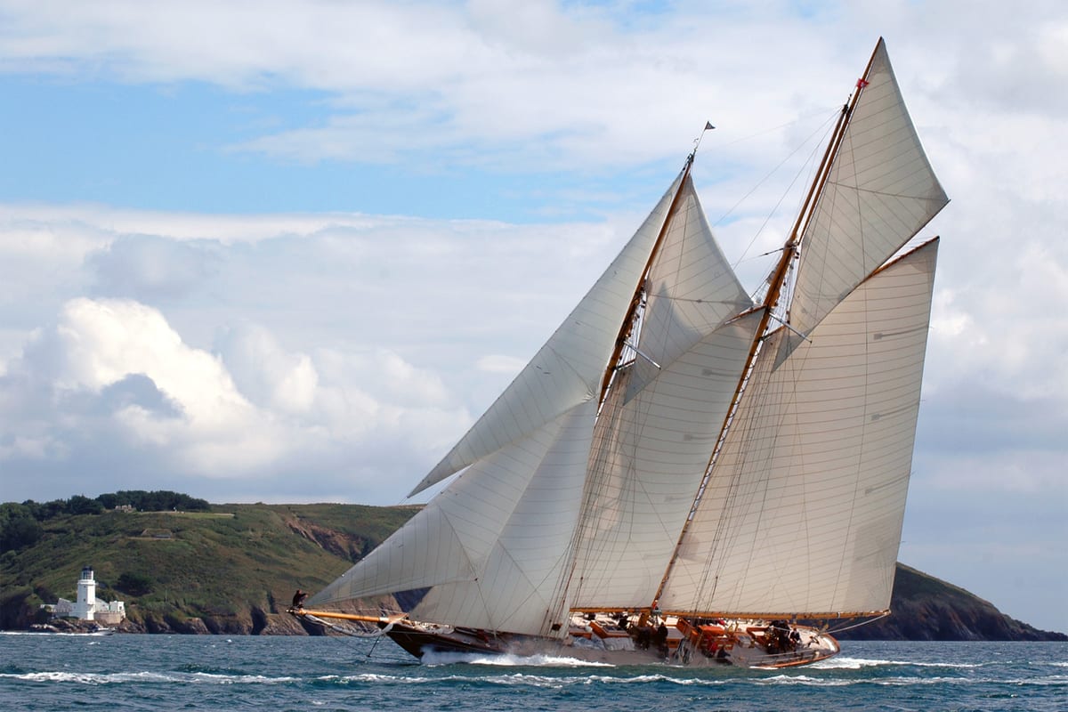 Classic sailing yacht Mariette heeling under full sail past St Anthony Lighthouse off the Cornish coast.