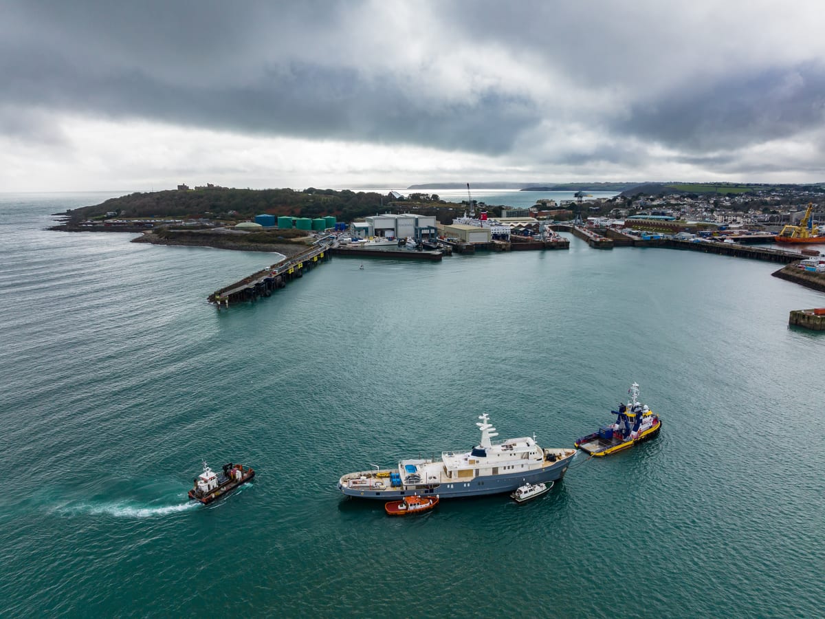 Superyacht Seawolf arriving in Falmouth Harbour, escorted by tugboats under cloudy skies.