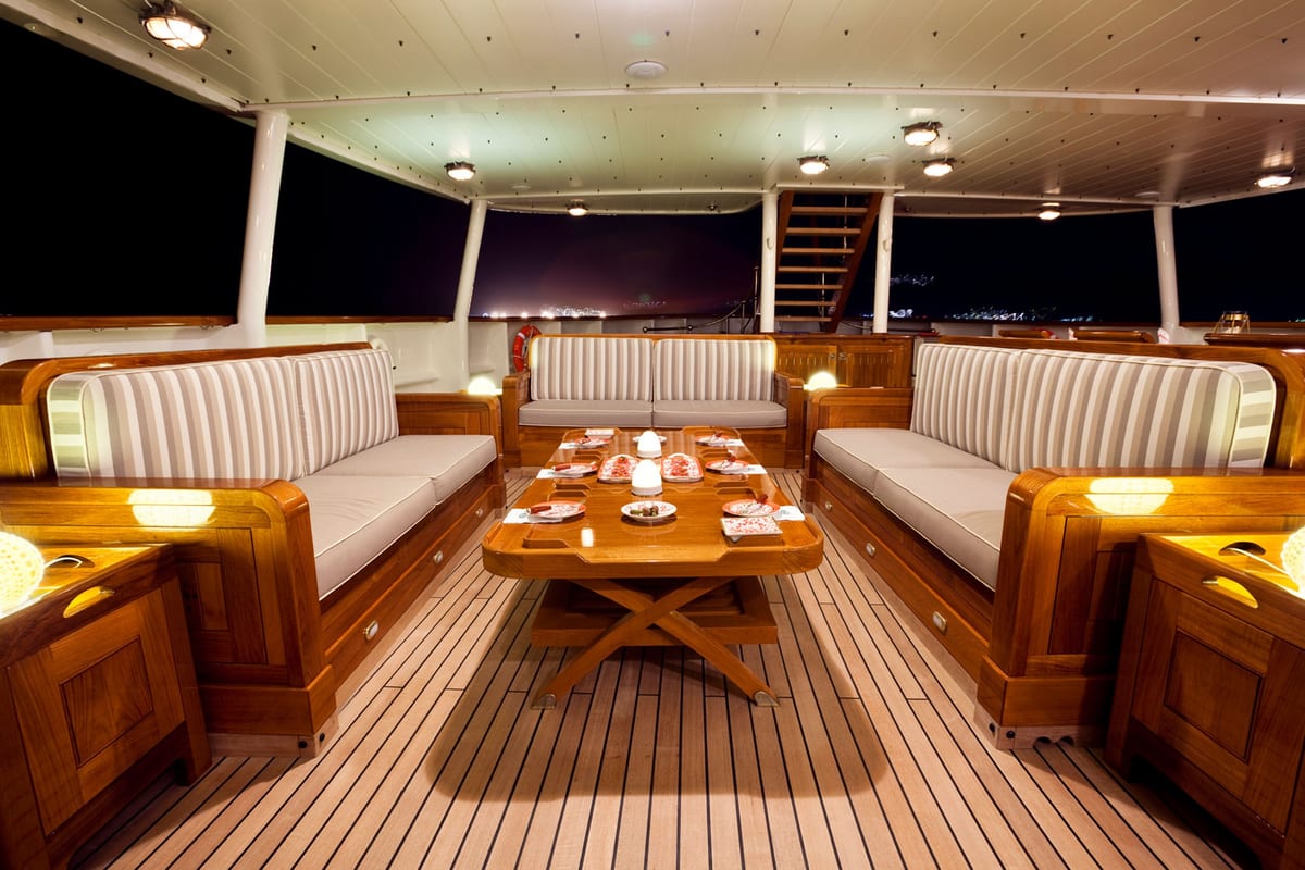 Evening lounge setup on STEEL’s aft deck with striped seating, wood furnishings and ambient lighting.
