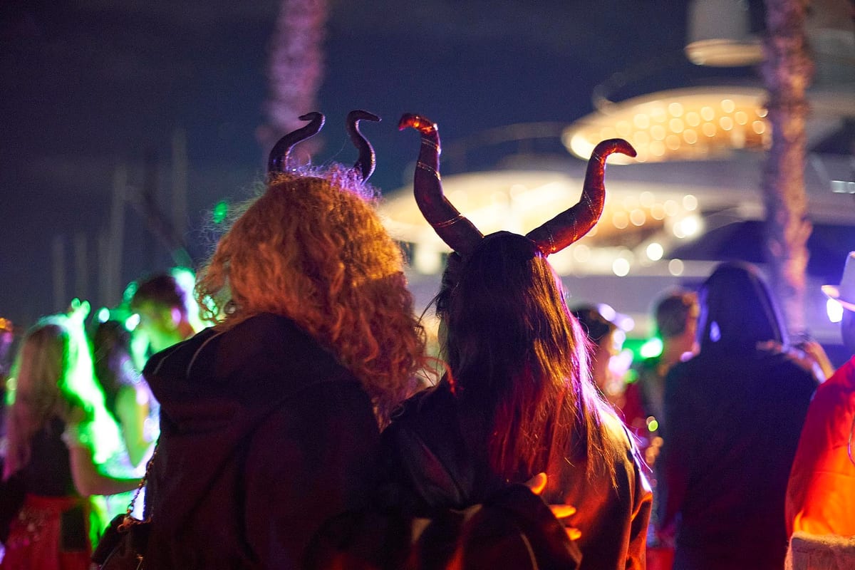 Guests in Halloween costumes with horned headpieces enjoying a lively party near a superyacht at night.