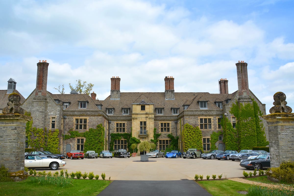 A collection of classic cars parked in front of Llangoed Hall, a grand ivy-covered country house in Wales.
