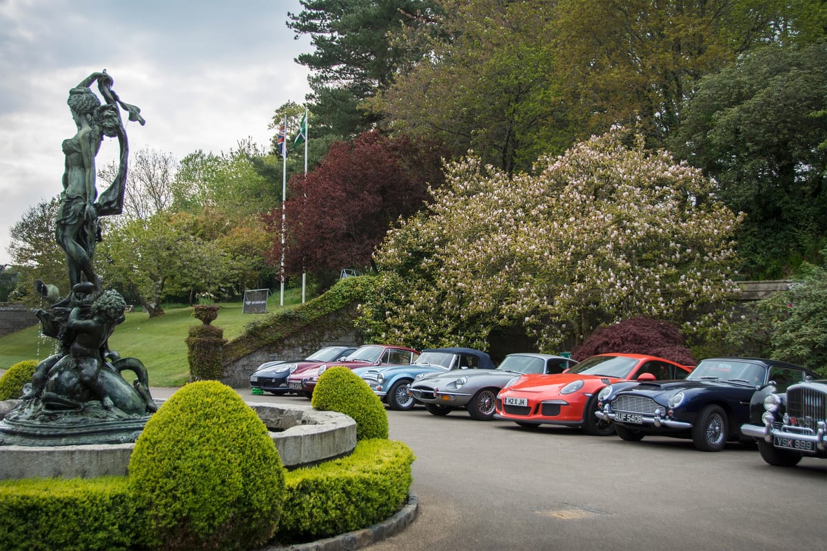 Line of classic cars parked beside a bronze fountain and manicured garden at Bovey Castle in Dartmoor National Park.