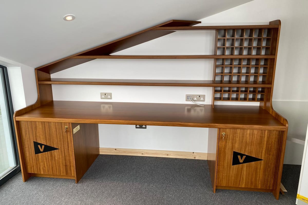 Custom-built wooden desk with integrated shelving and Flushing Sailing Club burgee detailing, installed in a race control room.