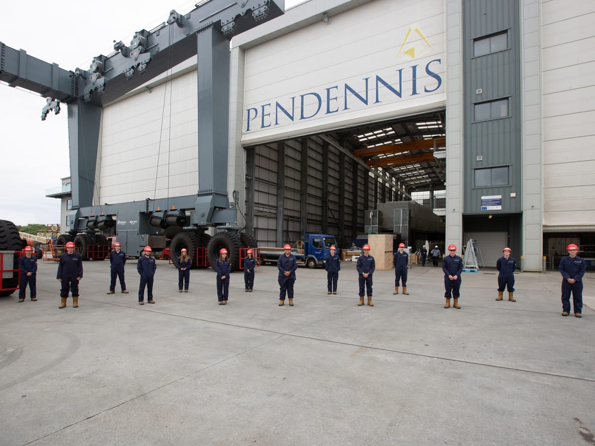 Pendennis Shipyard’s 2021 apprentice intake stands spaced apart outside the main facility, wearing uniforms and hard hats.