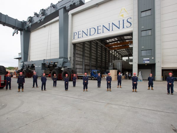 Pendennis Shipyard’s 2021 apprentice intake stands spaced apart outside the main facility, wearing uniforms and hard hats.