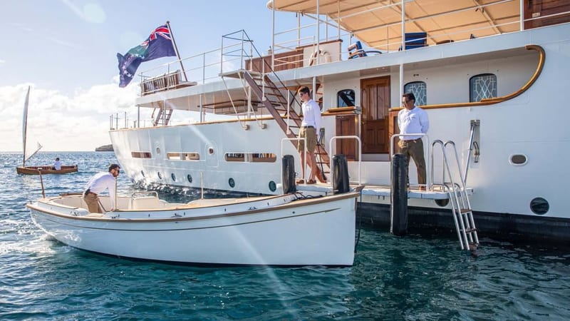 Cockwells tender alongside a classic Pendennis motor yacht, with crew preparing for boarding in calm coastal waters.