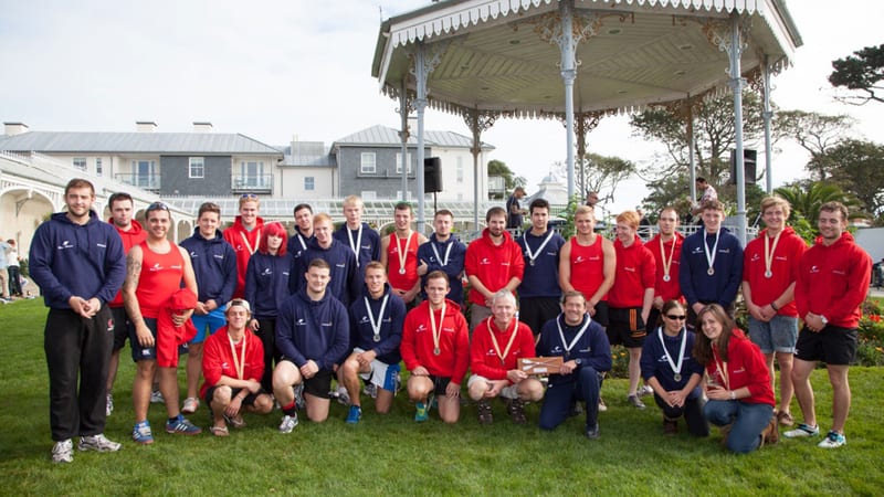 Pendennis team members wearing medals and branded hoodies gathered in front of a Victorian bandstand after a gig rowing race celebrating 25 years of the shipyard.