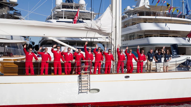 Red Arrows display team waving from a classic yacht alongside Pendennis crew, celebrating Pendennis Shipyard’s 30th anniversary.