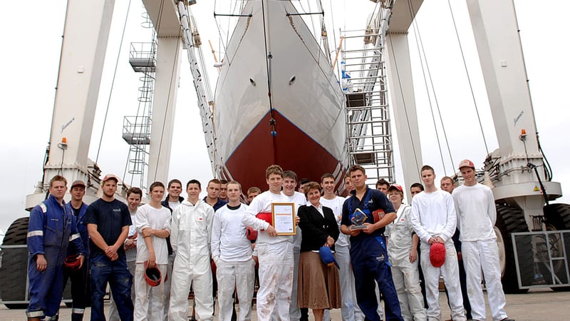 Group of Pendennis apprentices standing in front of a classic yacht in the hoist, marking the early days of the apprenticeship scheme.