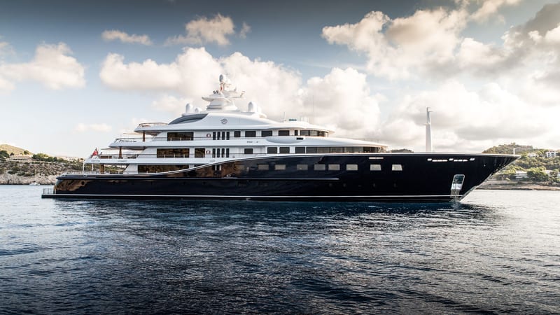 Superyacht Aquila cruising at sea, showcasing her distinctive dark blue hull and elegant white superstructure.