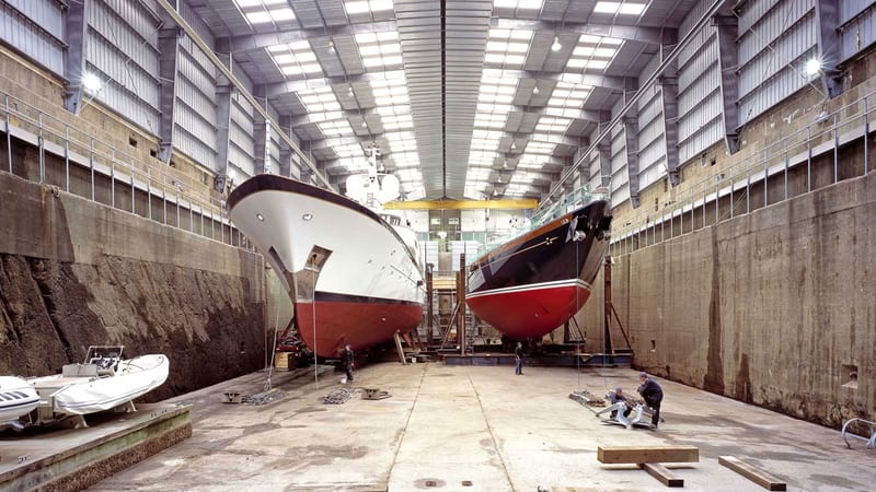 Two superyachts undergoing maintenance inside Pendennis Shipyard’s enclosed refit complex.