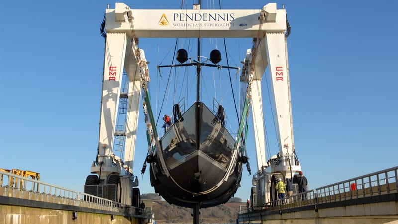 Black-hulled sailing yacht being launched by Pendennis’s 400-tonne travel hoist in Falmouth.