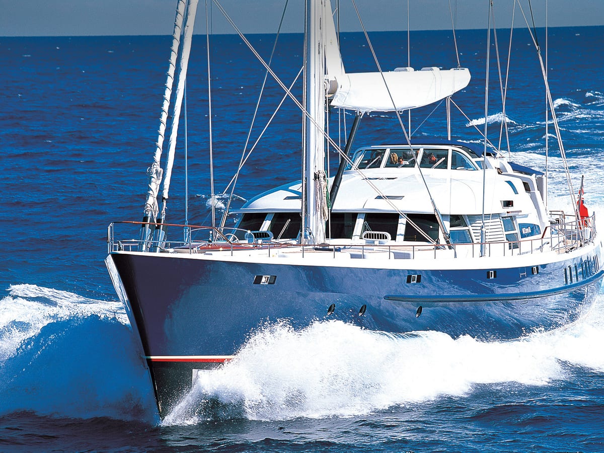 Sailing yacht MITseaAH powers through the waves under motor, with water spraying off the bow and a deep blue hull gleaming in the sun.