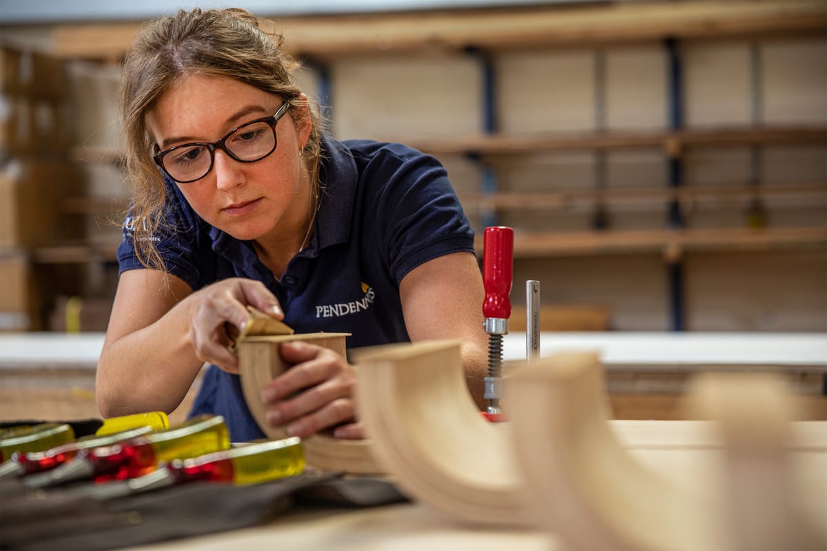 Craftsperson sanding a curved wooden component in the joinery workshop.