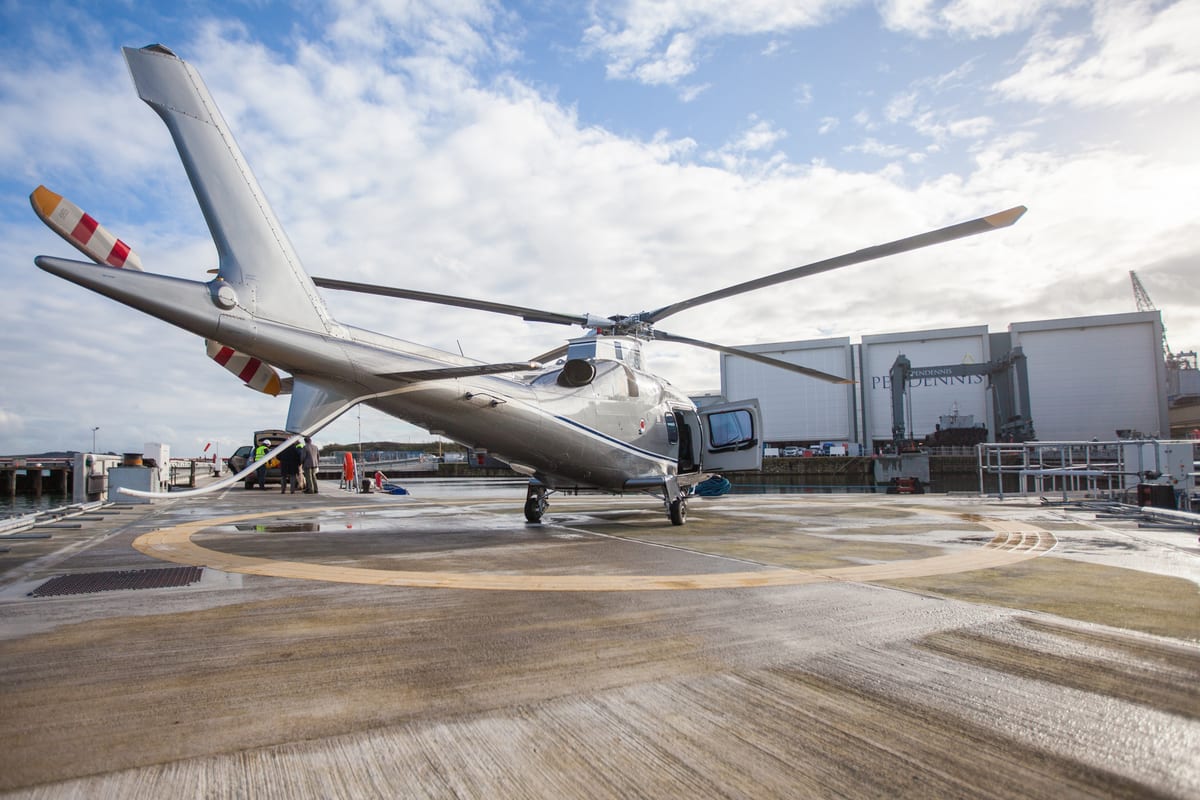 Helicopter parked on the Pendennis Shipyard helipad with main facilities visible in the background.