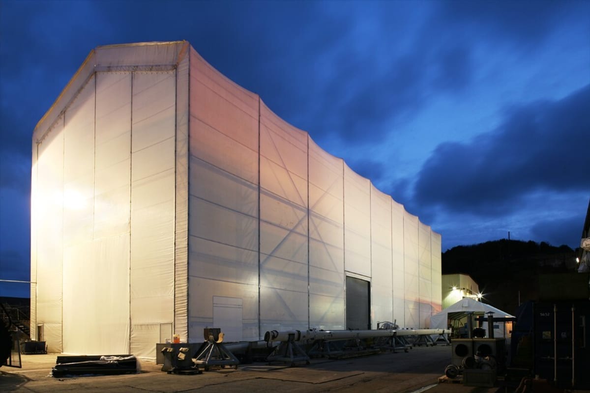 Large illuminated temporary structure at Pendennis Shipyard, known as the White House, lit up at night.