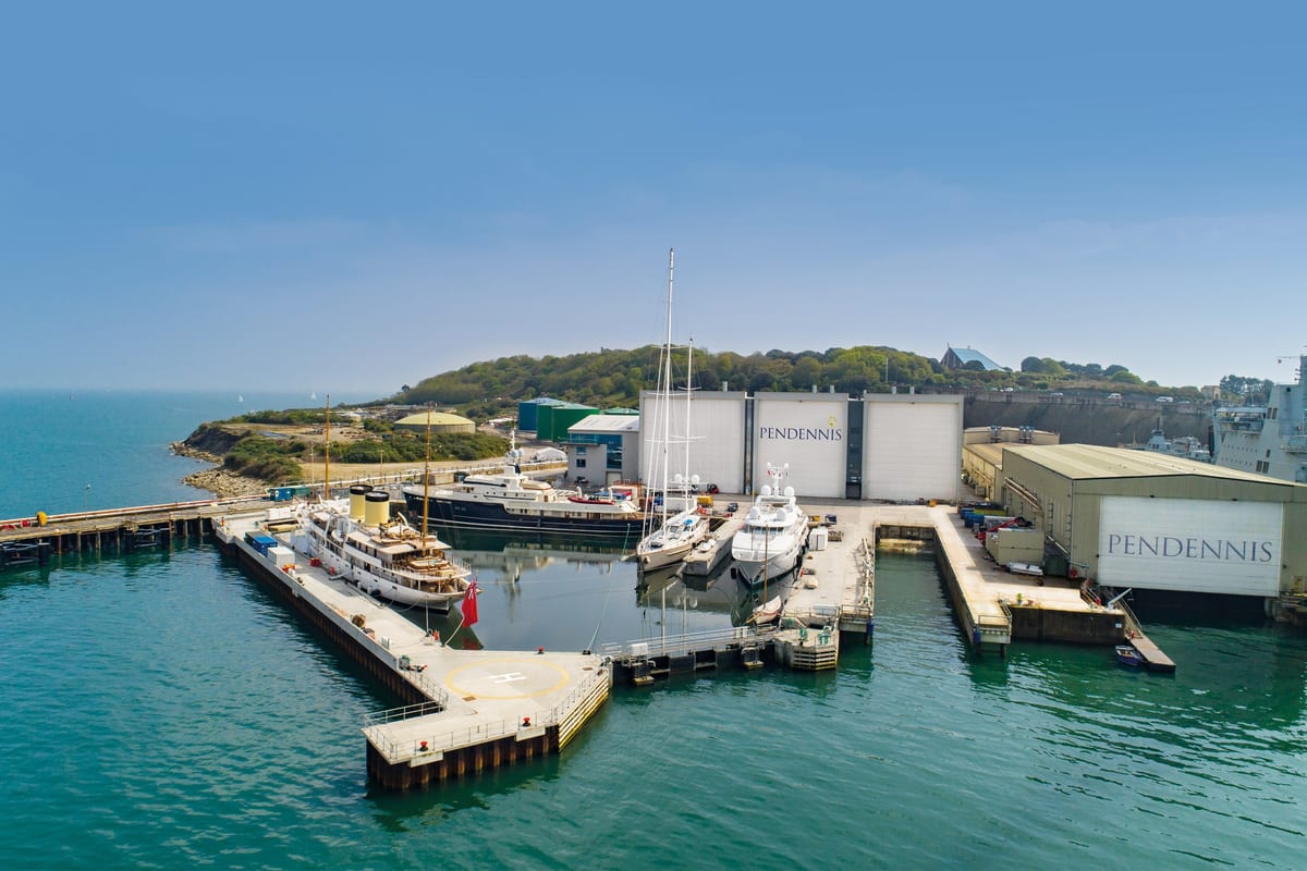 Aerial view of Pendennis Shipyard’s non-tidal wet basin with multiple superyachts docked under clear skies.