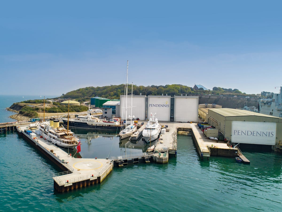 Aerial view of Pendennis Shipyard’s non-tidal wet basin with multiple superyachts docked under clear skies.