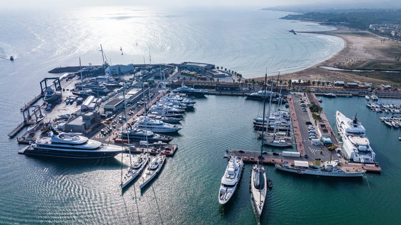 Aerial view of Pendennis Vilanova marina and shipyard on a bright day, with yachts berthed along multiple piers.