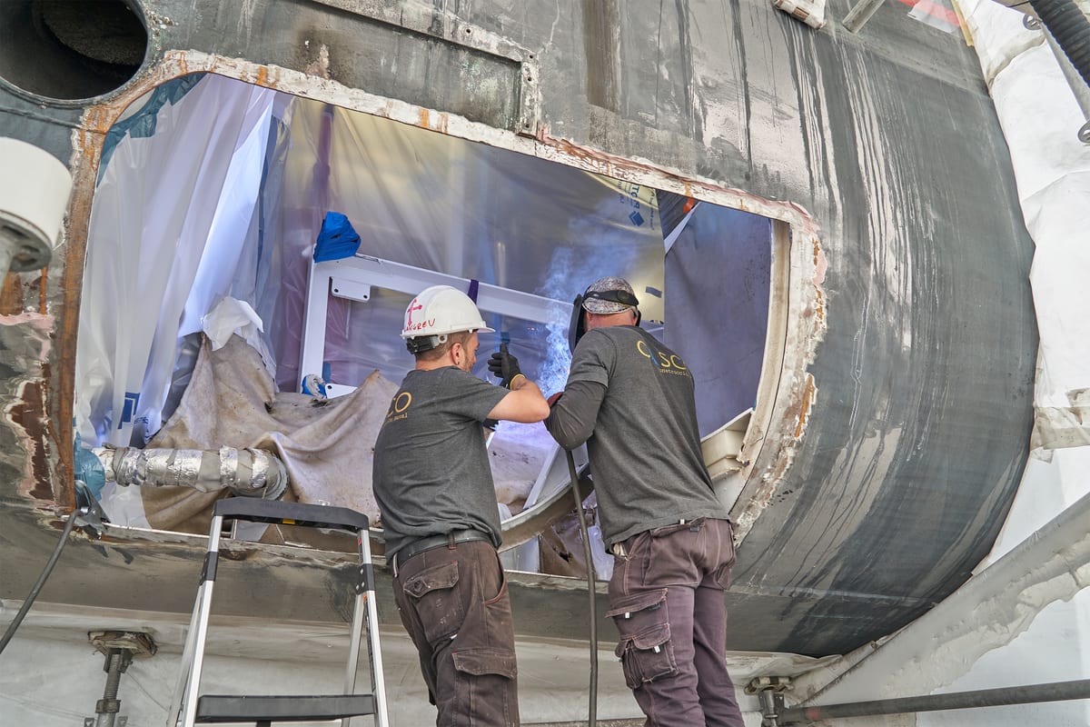 Two men working on the underside of a motor yacht