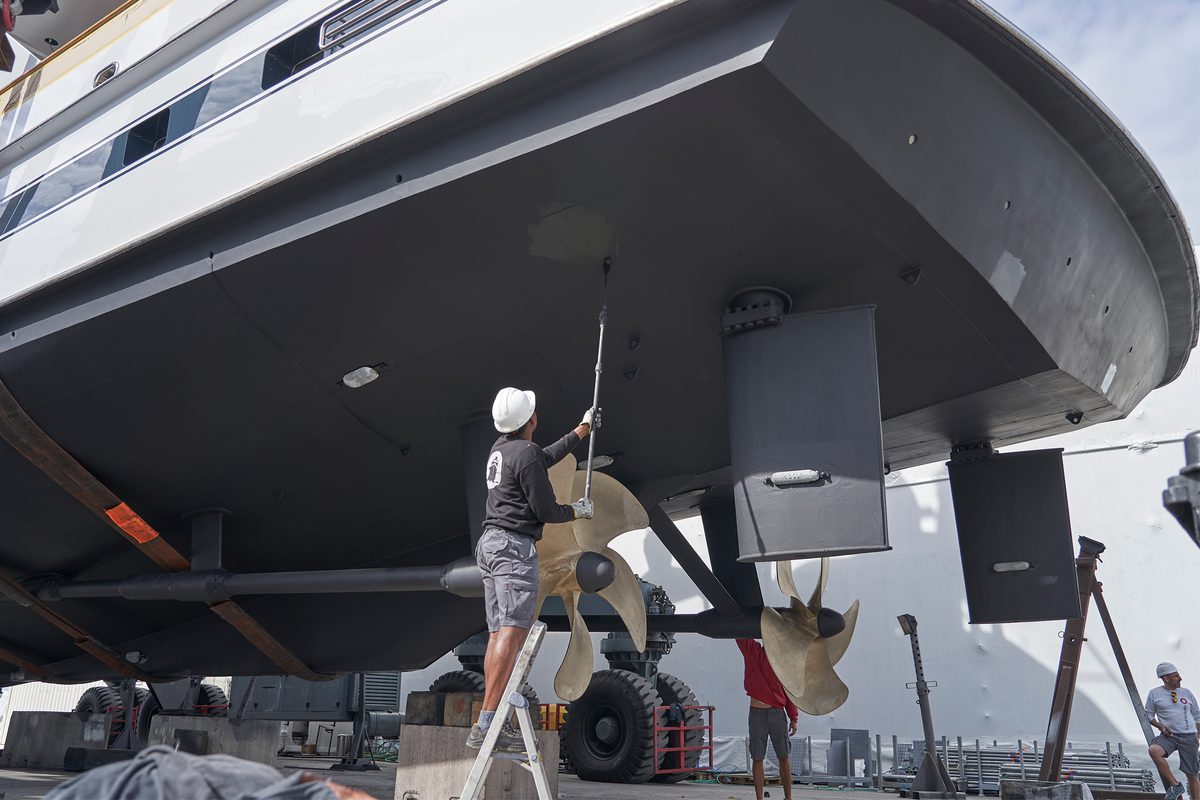 A man applies paint to the underside of a motor yacht using a roller