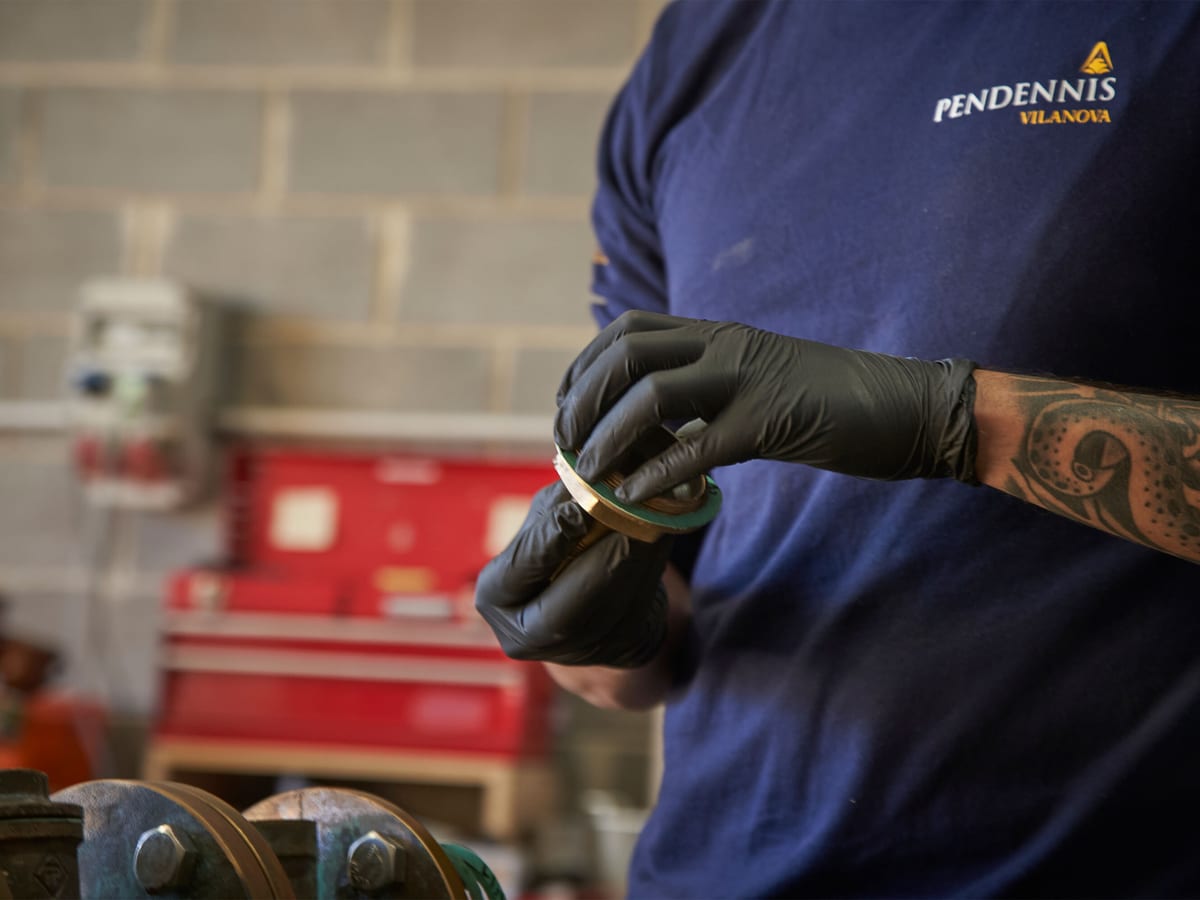 Pendennis Vilanova technician handling a precision engineering component in the workshop, wearing gloves and uniform.