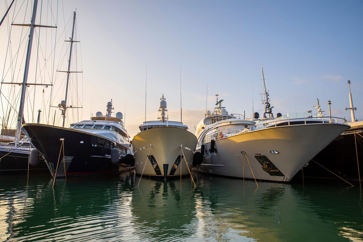 Multiple superyachts moored bow-to at Pendennis Vilanova marina during golden hour, with calm water and soft light.