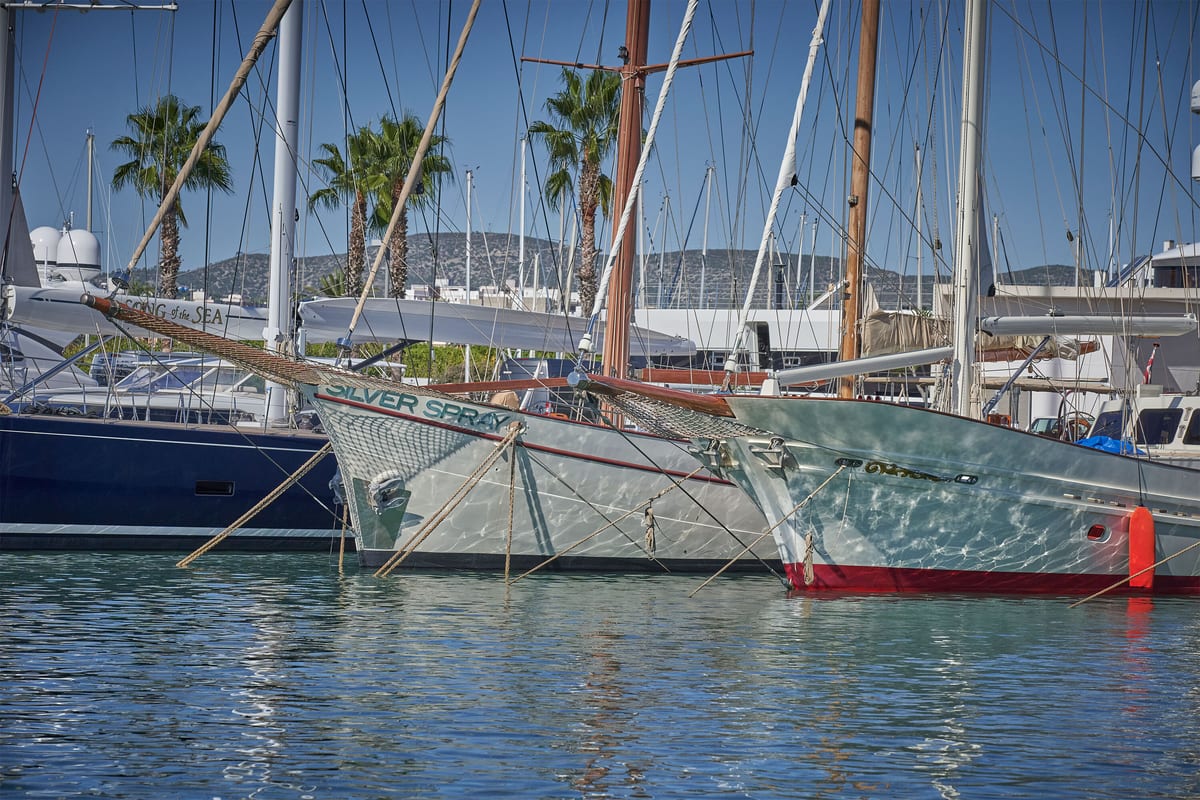 Classic sailing yacht Silver Spray moored at Pendennis Vilanova marina, with palm trees and hills in the background.