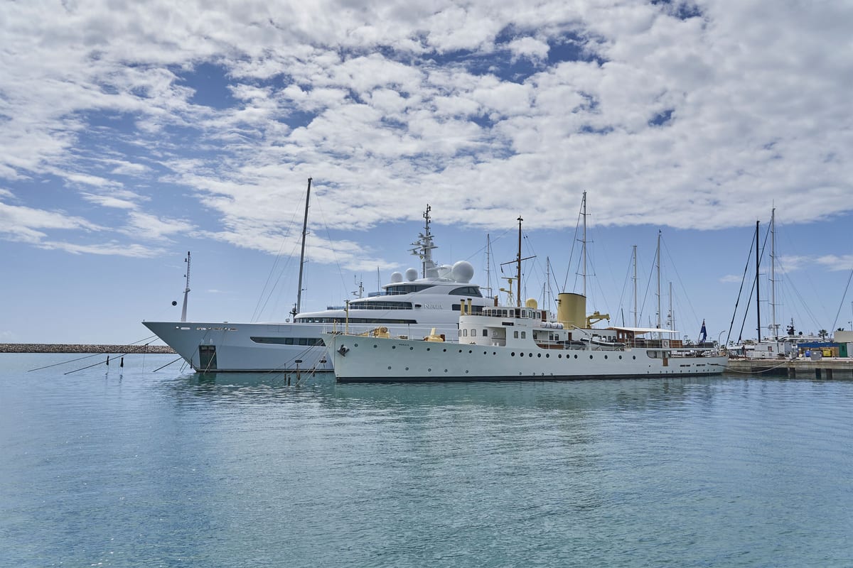 Two superyachts moored side by side at Pendennis Vilanova marina, with clear skies and calm waters.