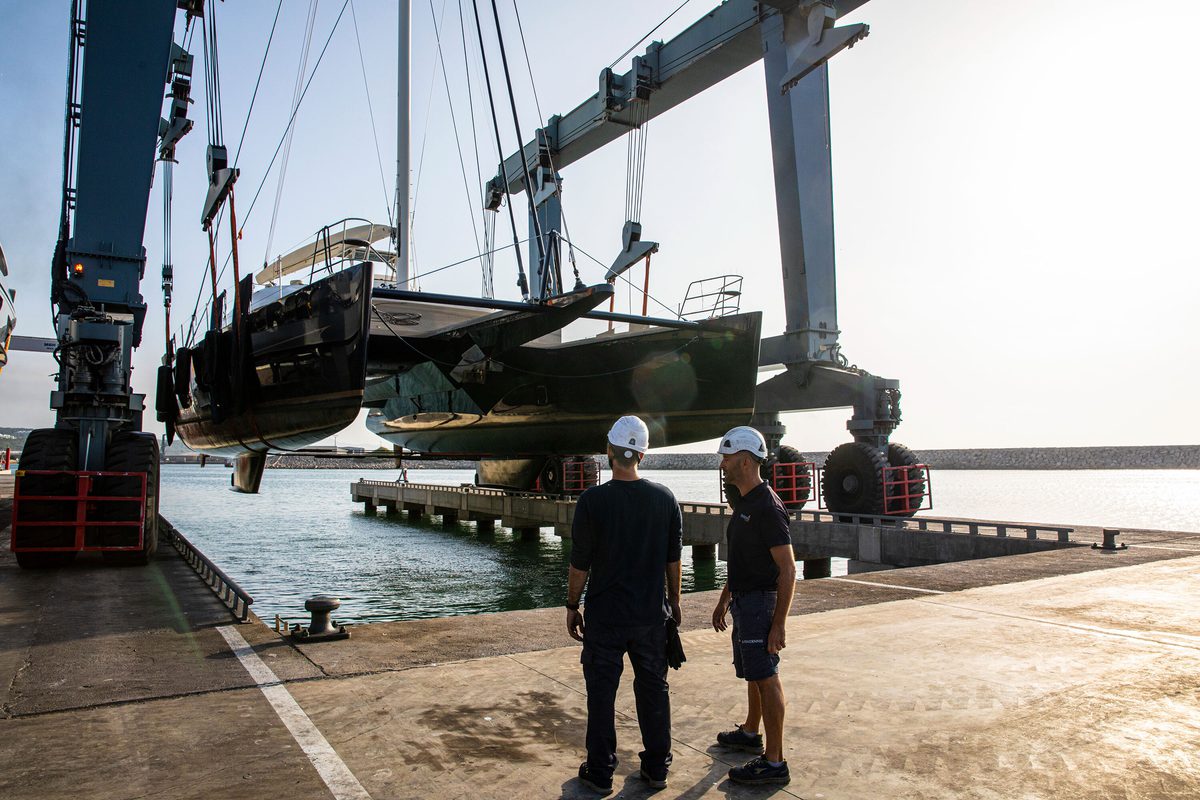 Two team members supervise a catamaran being lifted from the water by the Pendennis Vilanova travel hoist.