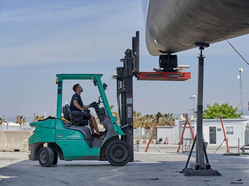 Pendennis Vilanova technician uses a forklift to position equipment beneath a yacht on land.