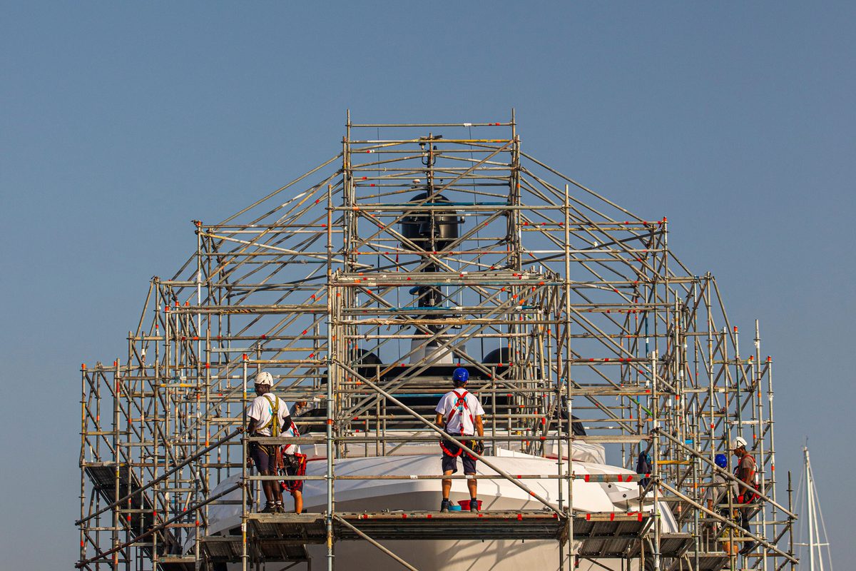 Workers on scaffold surrounding a superyacht at Pendennis Vilanova, carrying out refit or maintenance work.