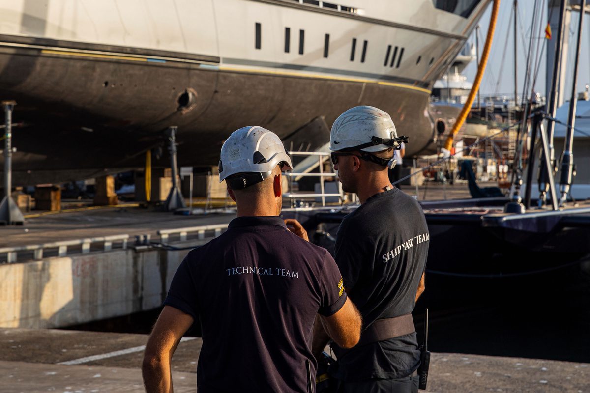 Pendennis Technical and Shipyard team members in discussion beside a superyacht undergoing maintenance at the Vilanova facility.