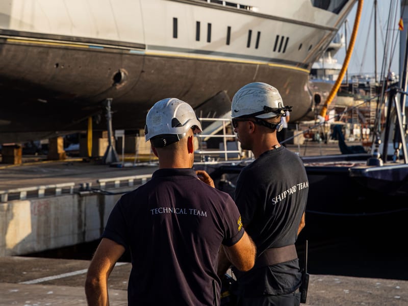Pendennis Technical and Shipyard team members in discussion beside a superyacht undergoing maintenance at the Vilanova facility.