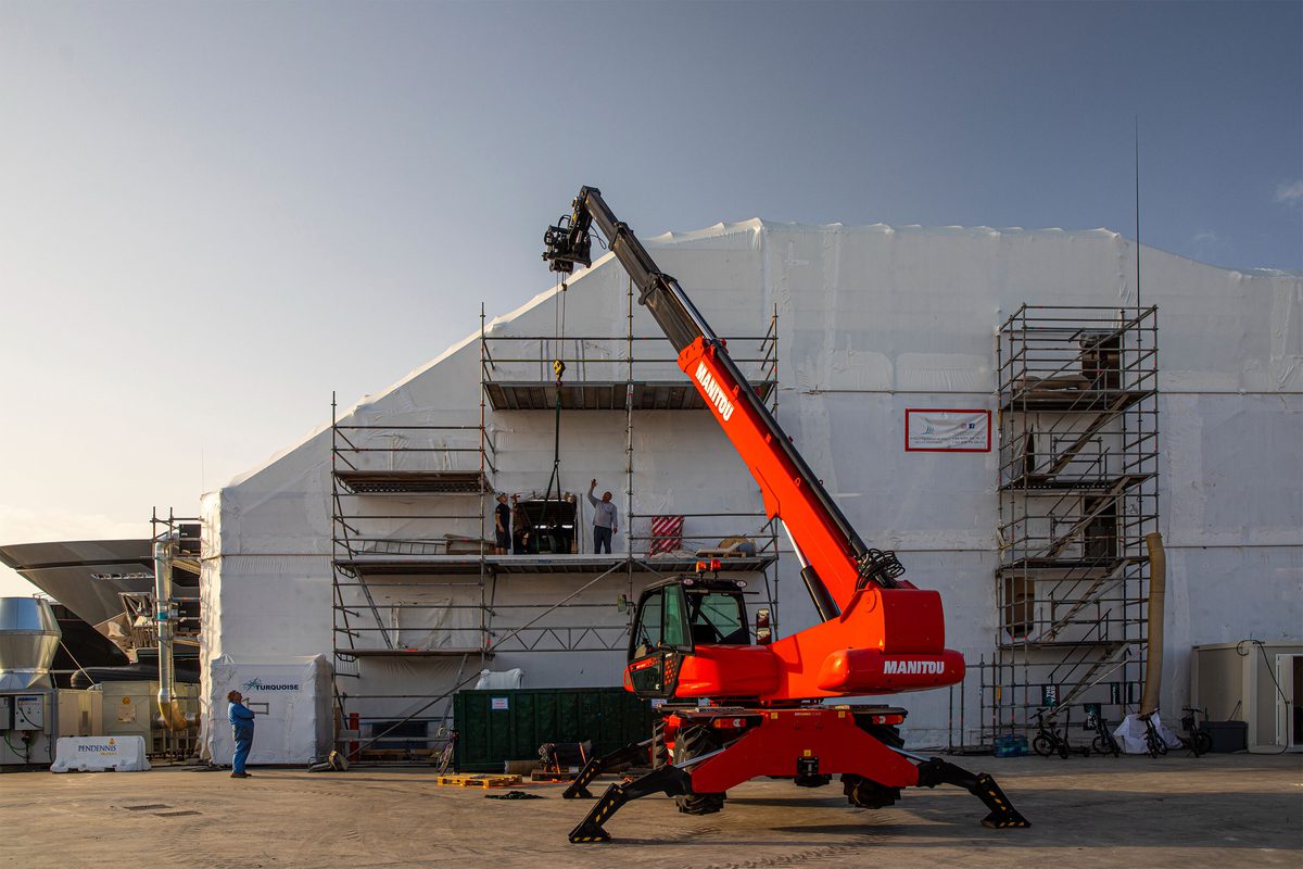 Red Manitou telehandler positioned beside scaffolded structure at Pendennis Vilanova facility during maintenance work.